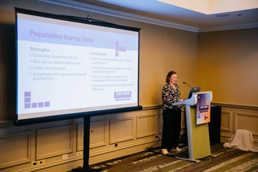 Emily Hoover presents, standing at a podium with a projection screen next to her.