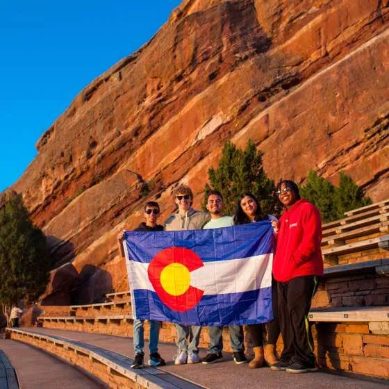 A group of people holds a Colorado flag near a mountain.