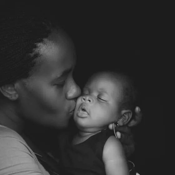 A Black mother kisses her infant child.