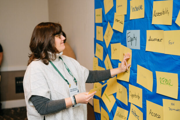 A Region 5 PHIG Convening attendee adds index cards to a board with other words considering what equity means in public health.
