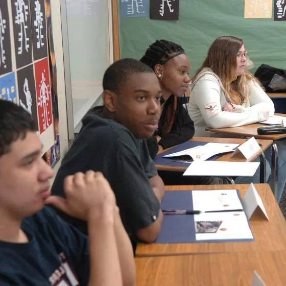 A group of teens sit at desks in a school classroom.